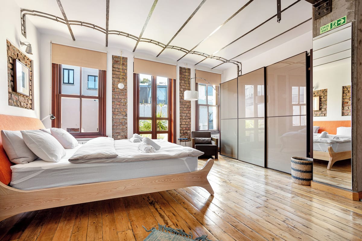 A modern bedroom with a wooden bed, large windows, and a view of the outside.