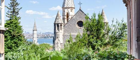 Una mesa de madera con individuales rojos, una maceta blanca con plantas verdes y vistas a una iglesia histórica con múltiples torres.