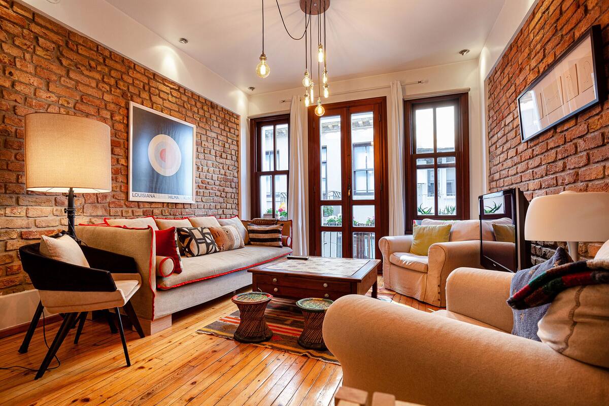 A cozy living room with a brick wall, wooden flooring, and a large window.