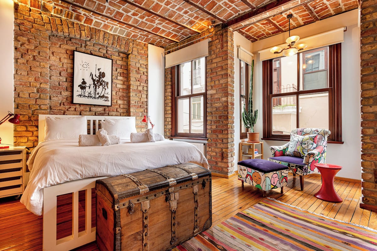 A bedroom with a large bed, a wooden trunk, a colorful rug, and a chair with a unique design.