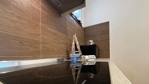 A kitchen with a black countertop, wooden backsplash, and a small island with a sink. - Cozy Apartment in the Heart of the Pinewood (Rosolina)