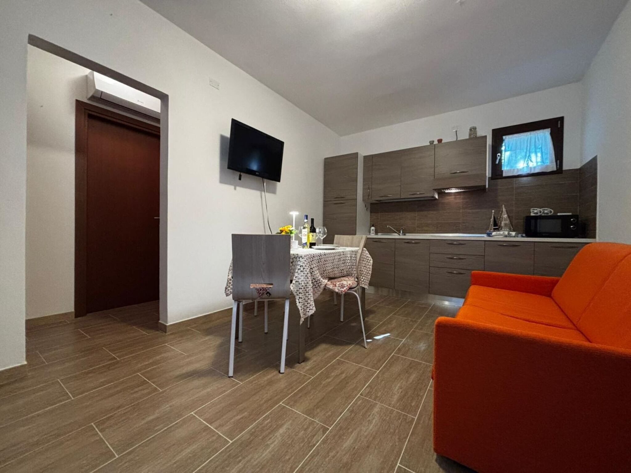 A compact living space with a dining area, kitchenette, and a TV mounted on the wall.