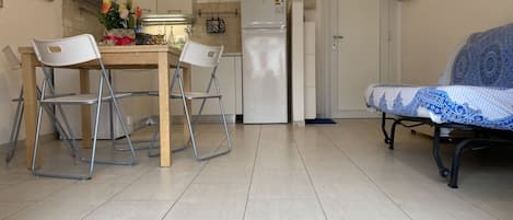 A compact kitchen with a dining table, two chairs, a sofa, and a refrigerator.