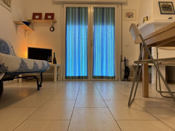 Una sala de estar con sofá, mesa de comedor, televisor y puerta corrediza de vidrio con cortinas.