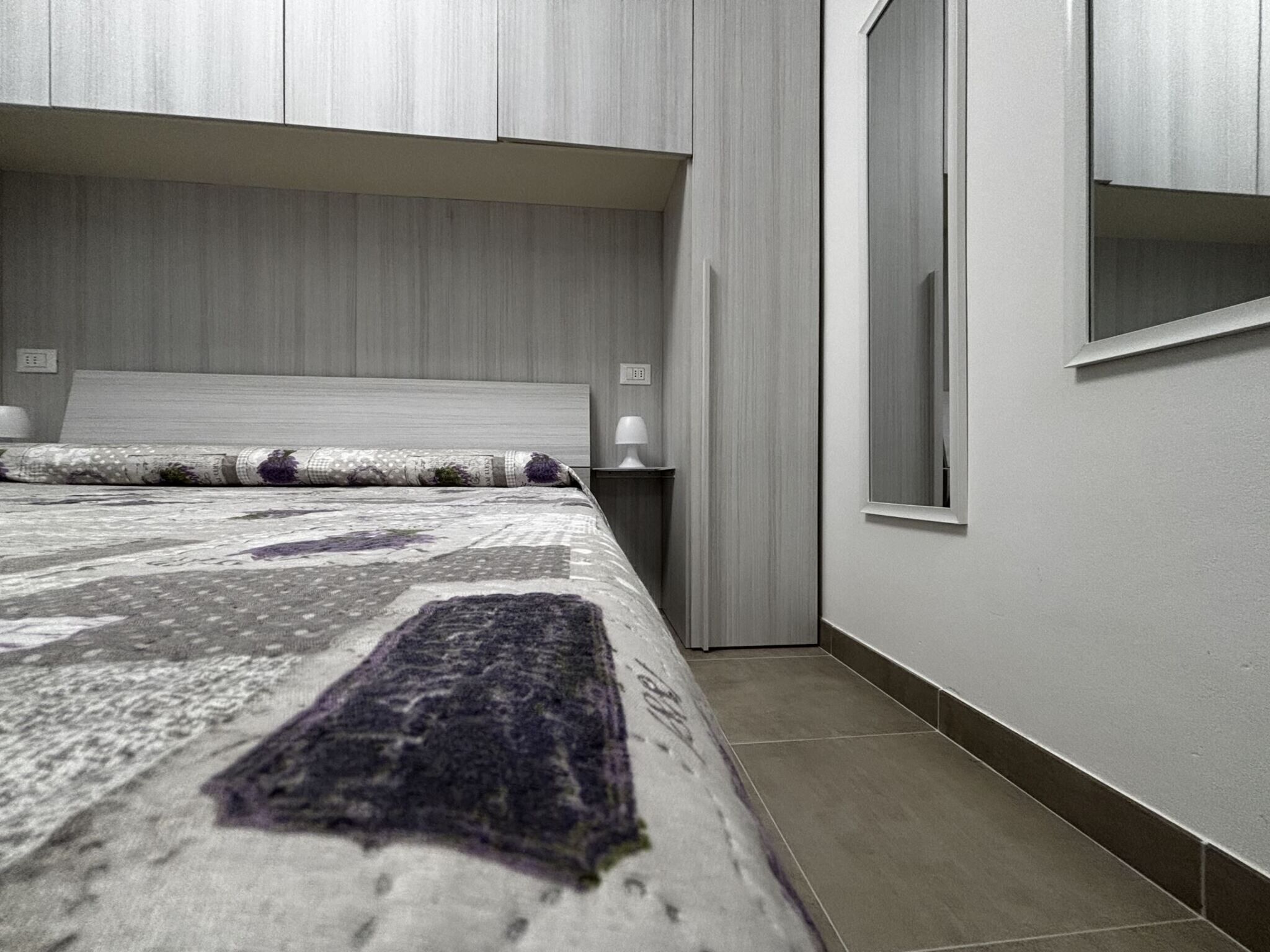 Ein Schlafzimmer mit einem Bett, einem Nachttisch, einer Lampe und einem Fenster.