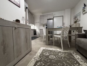 A modern kitchen with white cabinets, a dining area with a table and chairs, and a grey sofa. - Accommodation in the Vibrant Heart of Rosolina (Rosolina)