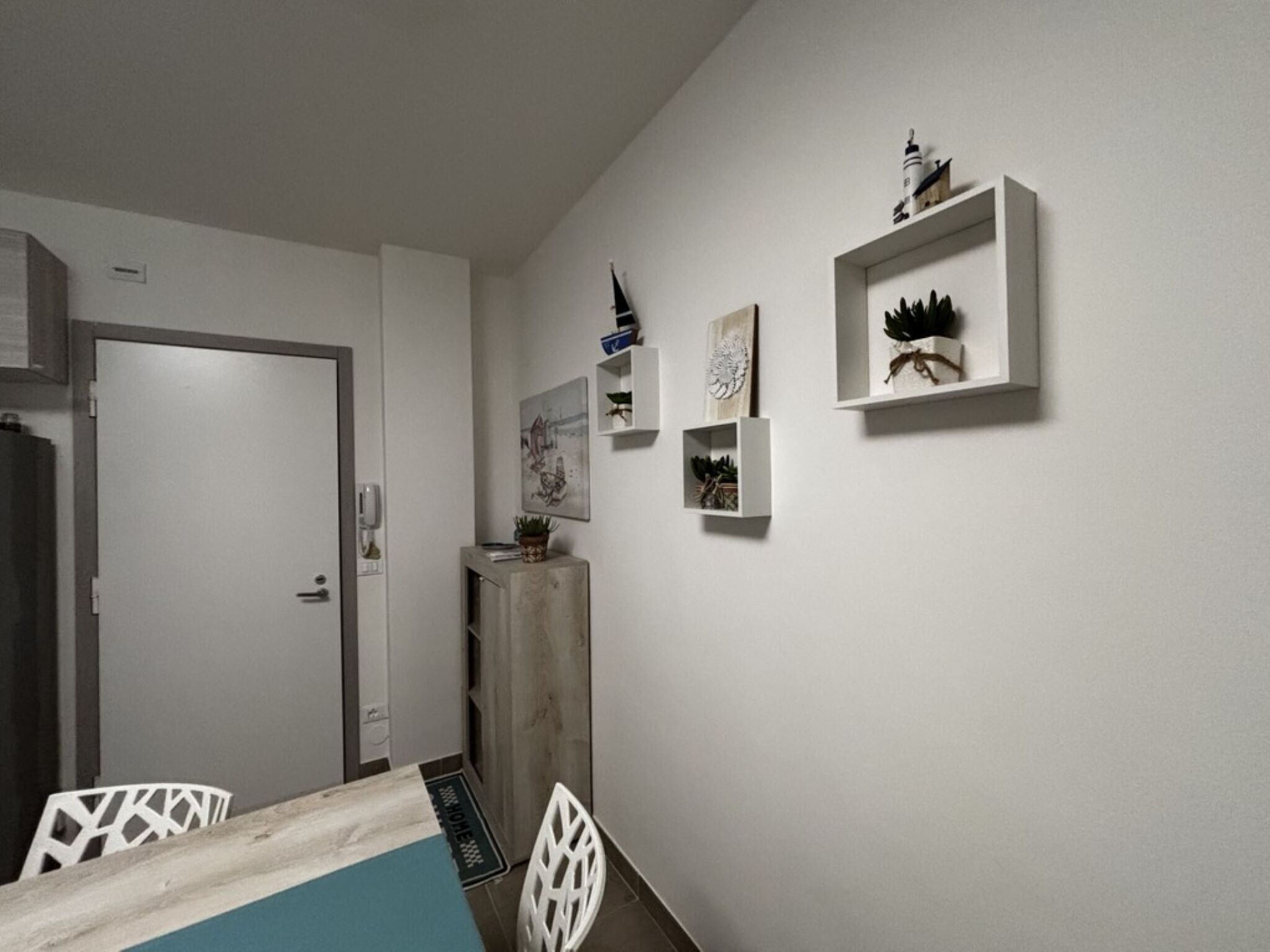 A modern, minimalist room with a bed, a desk, and a chair. There are wall-mounted shelves with decorative items.