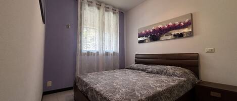 Un dormitorio con cama, cortinas, un cuadro y una mesita de noche.