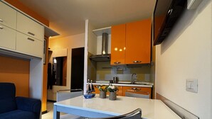 Moderni keittiö, jossa on valkoiset ja oranssit kaapit, ruokapöytä kahdella tuolilla sekä sininen sohva olohuoneessa.