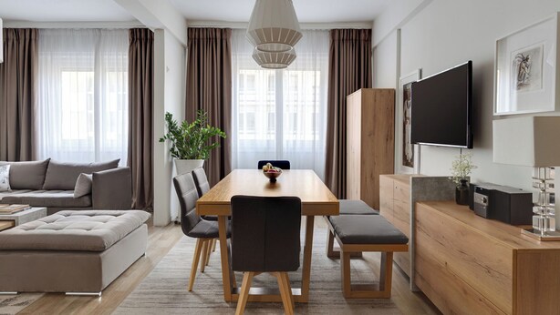 A modern living room with a wooden dining table, grey sofa, and a flat-screen TV mounted on the wall. - Syntagma Spotlight Residence, Bill & John Apartments & Villas (Athens)