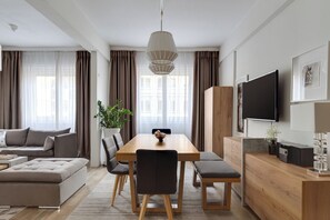 A modern living room with a wooden dining table, grey sofa, and a flat-screen TV mounted on the wall. - Syntagma Spotlight Residence, Bill & John Apartments & Villas (Athens)