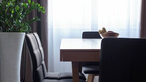 A dining area with a wooden table, black chairs, a potted plant, and a bowl of fruit. - Syntagma Spotlight Residence, Bill & John Apartments & Villas (Athens)