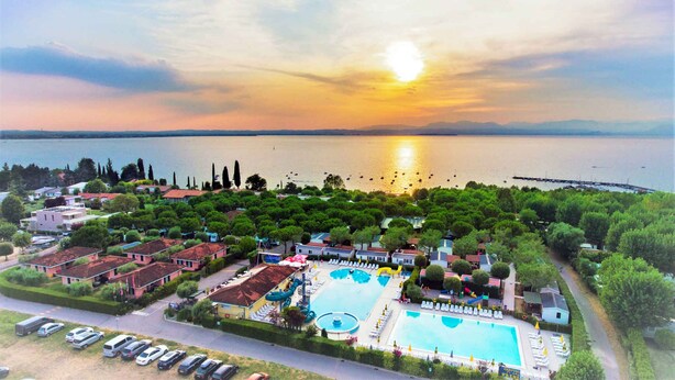 Un complex turístic amb una gran piscina, tobogan aquàtic i vista cap al capvespre sobre un llac.