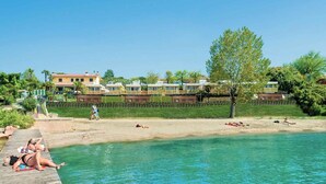 Una platja amb aigua cristal·lina, un pont de fusta i una filera de cases al fons.