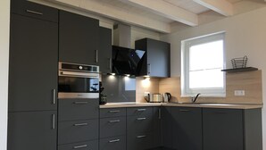 Une cuisine moderne avec des meubles de rangement aux couleurs sombres, un four encastré et une fenêtre qui laisse entrer la lumière naturelle.