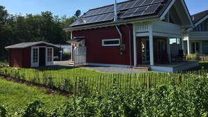 Une maison rouge dotée de panneaux solaires, d’un petit garage attenant et d’un jardin bien entretenu.