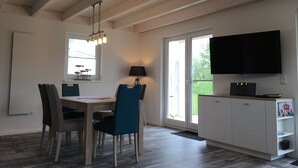 Une cuisine moderne avec un coin repas, un téléviseur fixé au mur et une grande fenêtre qui laisse entrer la lumière naturelle.