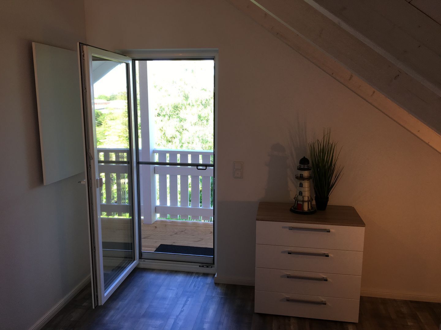 Ein Zimmer mit einer Schiebetür und Zugang zu einer Terrasse, einem weißen Schminktisch und einem Blumentopf.