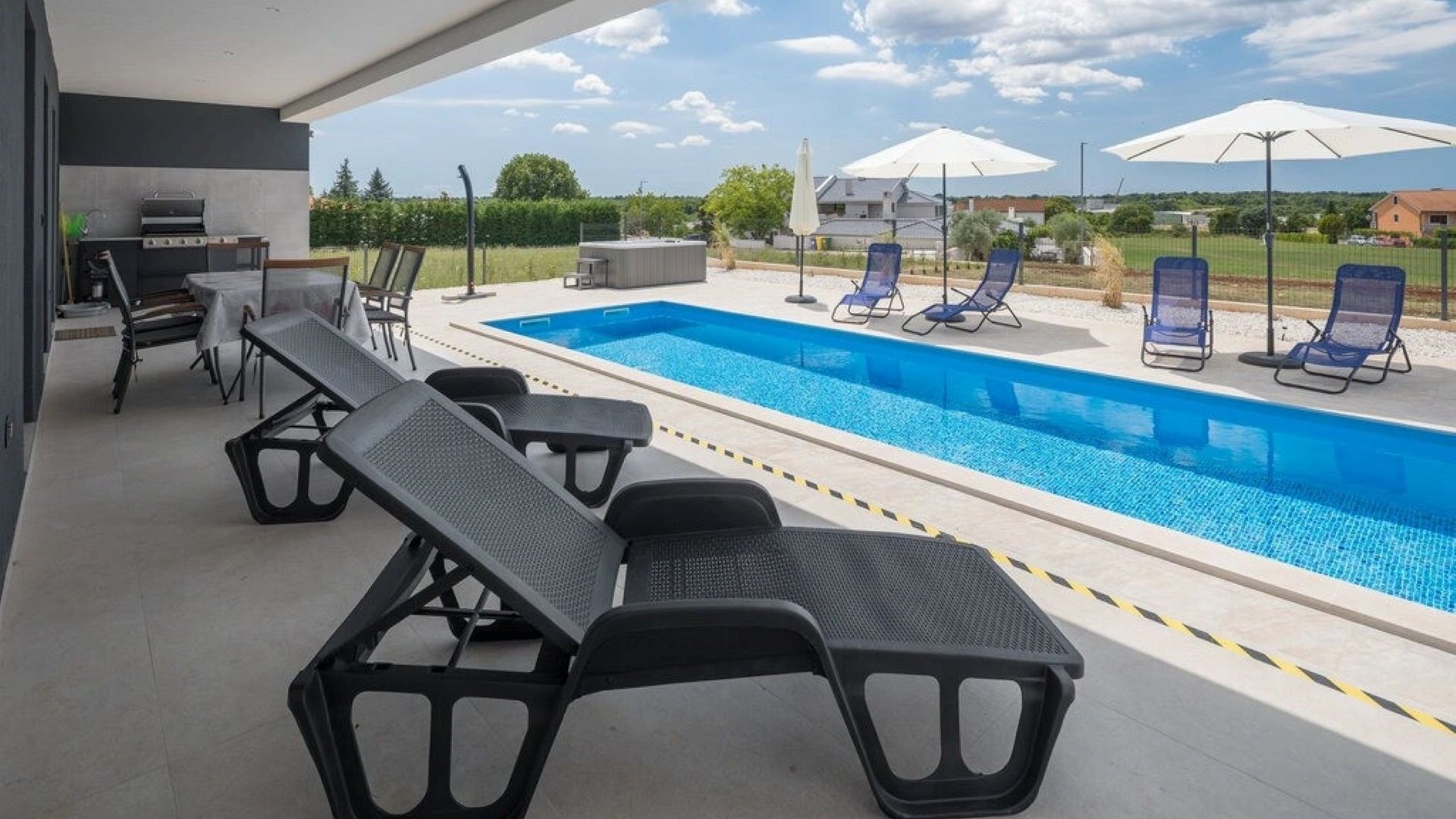 Un espace aménagé au bord de la piscine, avec des chaises longues, un jacuzzi et des parasols.