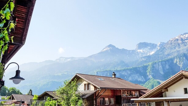 Un pueblo de montaña con casas de madera tradicionales, una farola de forma de campana y vistas a montañas nevadas.