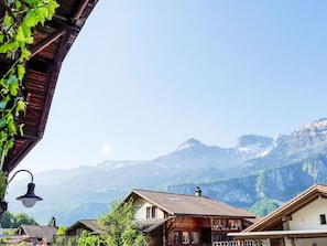 Un village de montagne aux maisons traditionnelles en bois, doté de lampadaires en forme de cloche, et offrant une vue sur des montagnes aux sommets enneigés.