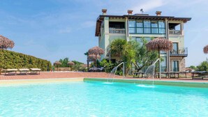 Una piscina con fuente, sillas de descanso y un edificio con balcones y ventanas amplias.