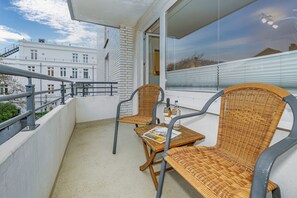 A balcony with wicker chairs, a small table, and a bottle of liquor. - Dünenburg Apartment 15 - Holiday apartment with balcony near the beach in the heart of (Sylt)