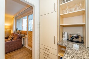 A compact kitchen with a toaster, a coffee maker, and a glass shelf with wine glasses. - Dünenburg Apartment 15 - Holiday apartment with balcony near the beach in the heart of (Sylt)