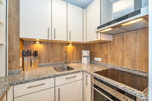 A modern kitchen with white cabinets, a granite countertop, a built-in stove, and a coffee maker. - Dünenburg Apartment 15 - Holiday apartment with balcony near the beach in the heart of (Sylt)