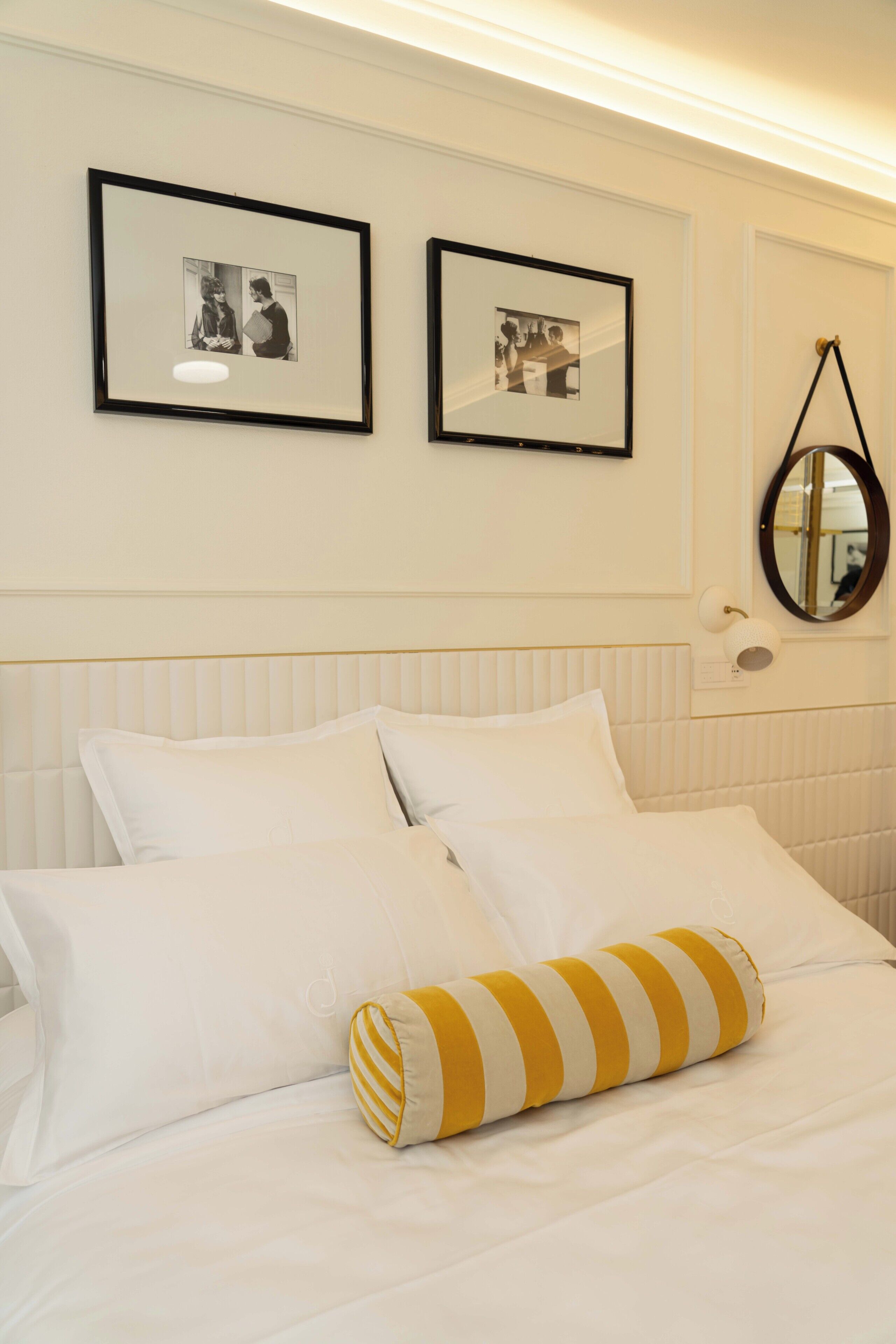 Een hotelkamer met een bed, wit beddengoed, twee ingelijste foto's aan de muur, een spiegel en een gestreept kussen.