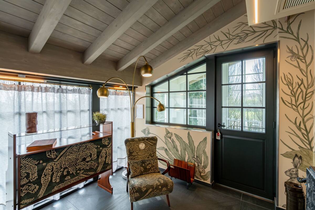 Une pièce avec un plafond en bois, une grande fenêtre, un fauteuil à motifs, un bureau en verre et une fresque murale.