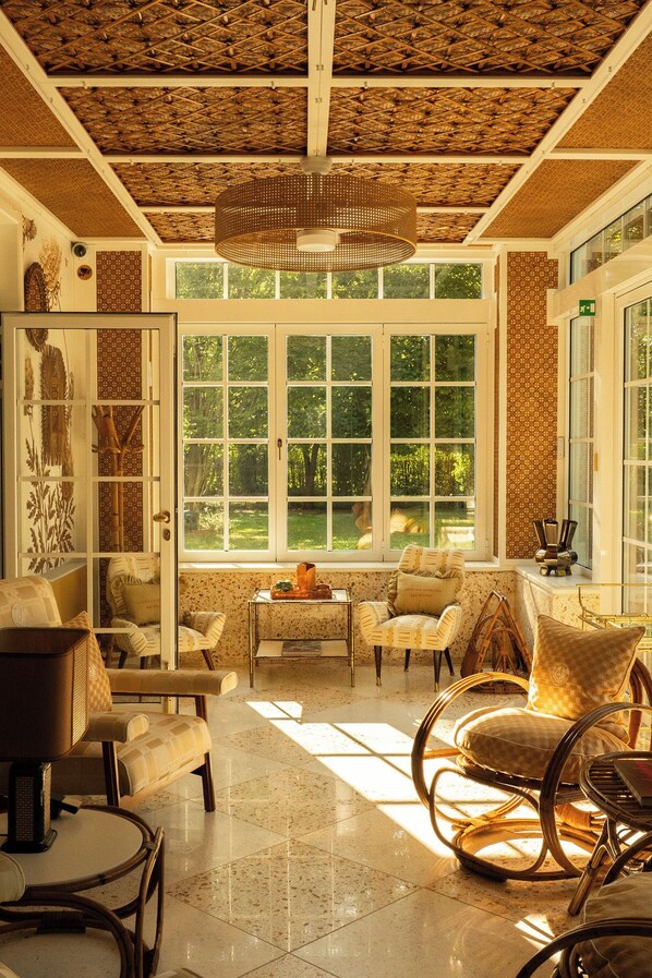 A sunlit room with a large window, wicker furniture, and a decorative ceiling. - Maison Chambre & Jardin (San Martino in Rio)