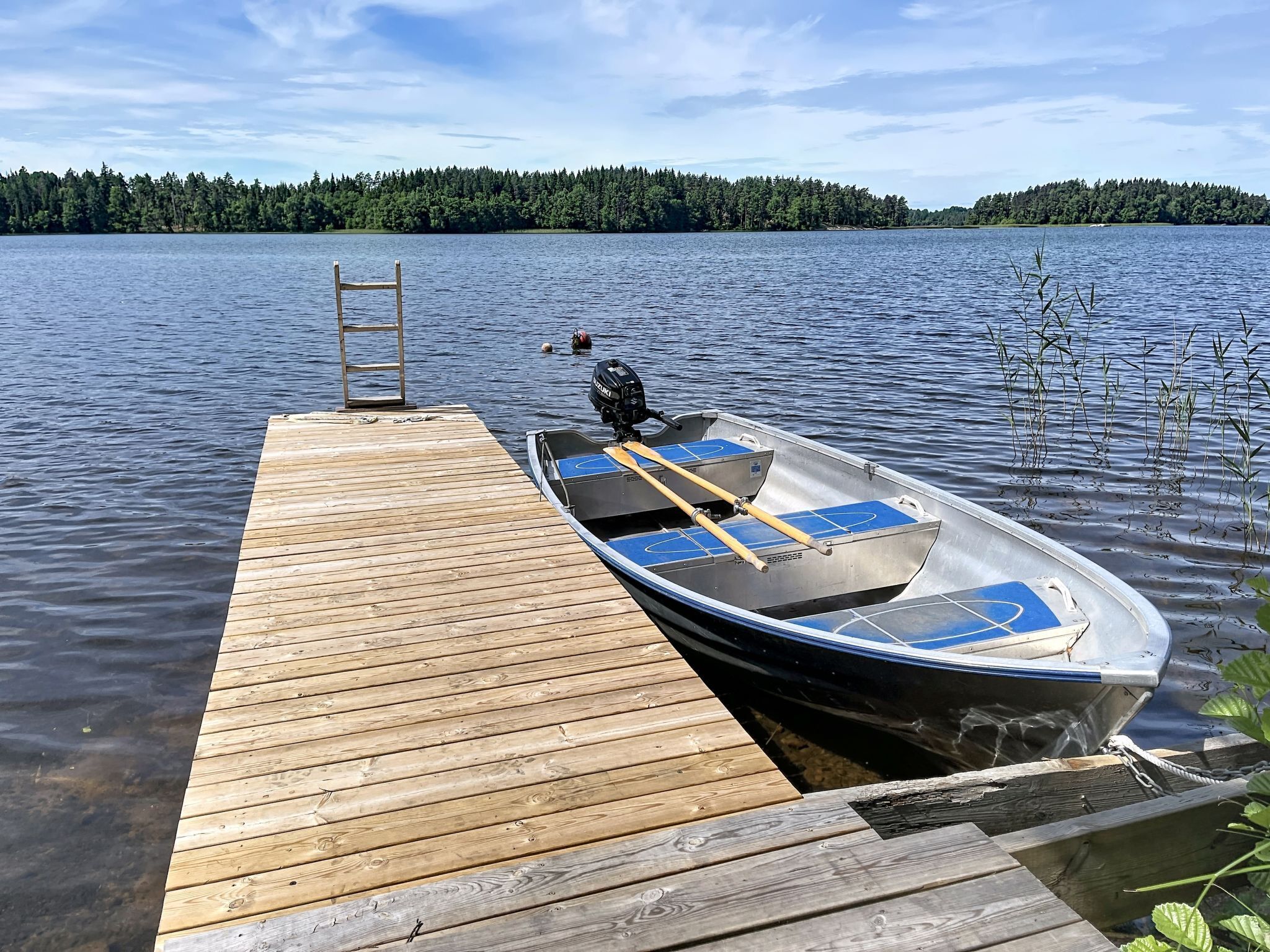 A wooden dock extending into a calm lake with a rowboat docked at the end.