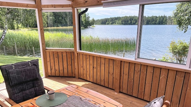 Een houten terras met een tafel en stoelen, met uitzicht op een meer met een bebost oever.