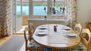 Een eetruimte met een tafel voor vier personen, stoelen, een kroonluchter en uitzicht op een meer door grote ramen.