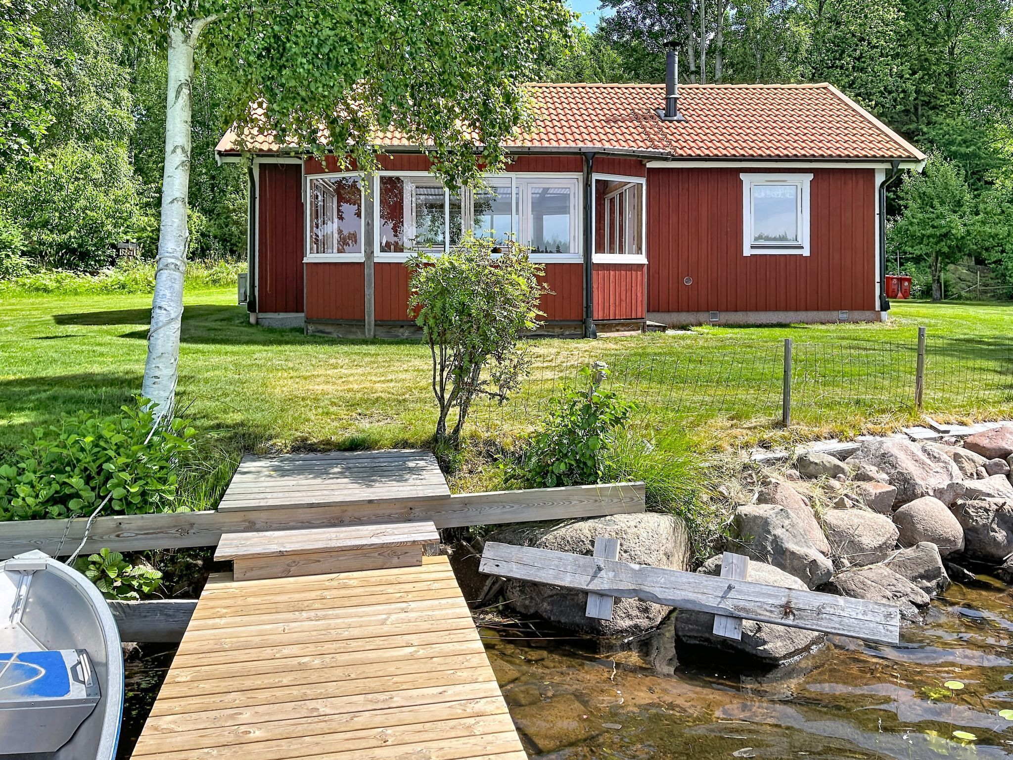Una casa de madera roja con un muelle que llega a un pequeño estanque, rodeada de follaje.