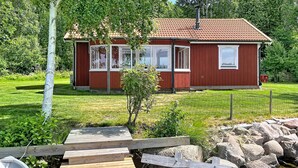 Een rode houten woning met een steiger die uitkomt bij een klein vijvertje, omringd door groen.