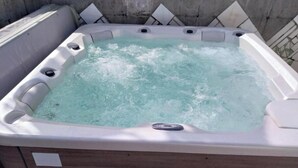 Ein Whirlpool mit Holzunterbau und weißer Außenverkleidung, umgeben von einer Betonmauer mit diamantförmigen Mustern.