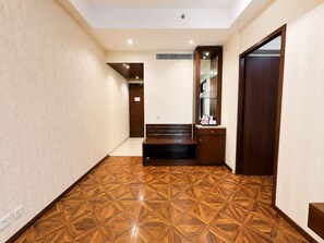 A hallway with patterned wooden flooring, a bench, a mirror, and a door. - Golden Tulip Kukas Jaipur (Amer)
