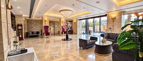 A spacious lobby with a marble floor, a grand chandelier, and a seating area with sofas and a coffee table.