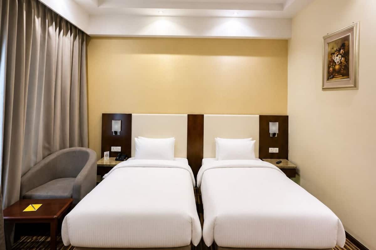 Habitación de hotel con dos camas, un escritorio, una silla, piso de madera y un cuadro en la pared.