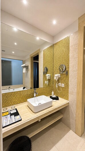 A modern bathroom with a large mirror, a white sink, and two hair dryers mounted on the wall. - Golden Tulip Kukas Jaipur (Amer)
