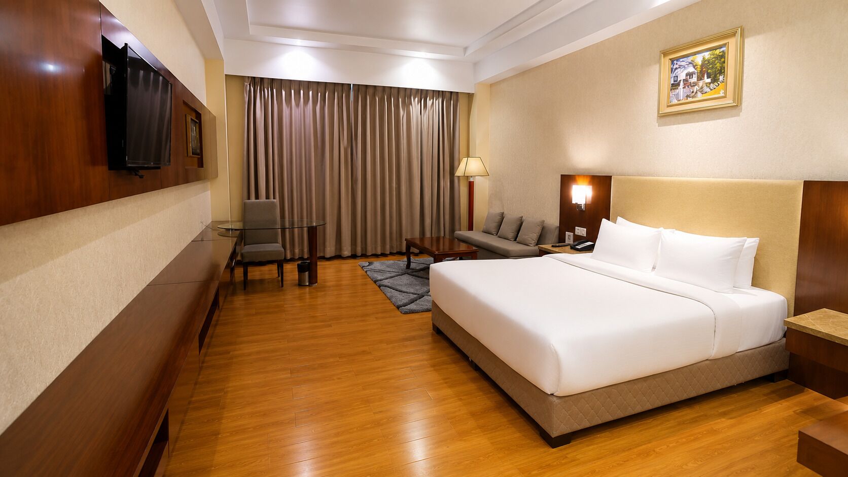A hotel room with a large bed, a desk, a chair, a TV, and a window with curtains.