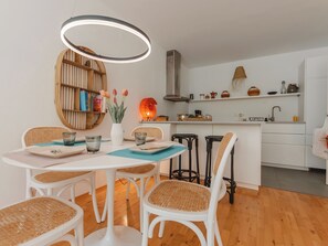 Uma cozinha moderna com armários brancos, uma mesa redonda de madeira com quatro cadeiras e um lustre.