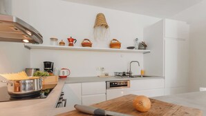 Eine moderne Küche mit weißen Schränken, einer Edelstahl-Dunstabzugshaube, einem Holzschneidebrett mit Messer und Zwiebel sowie verschiedenen Küchenutensilien auf Arbeitsfläche und Regalen.
