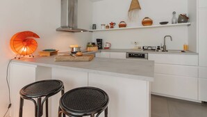 Eine moderne Küche mit weißen Schränken, einer Edelstahl-Dunstabzugshaube, einer Holzinsel mit Barhocker und einem Wandkorb.