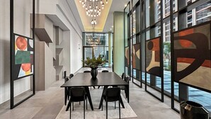Une salle de conférence moderne, dotée d’une longue table, de chaises, d’un lustre et de grandes fenêtres ornées d’œuvres d’art abstraites.