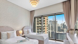 Une chambre d’hôtel avec deux lits, une vue sur la ville, un lustre moderne et une grande fenêtre avec des rideaux.