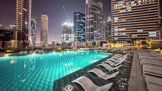 Une piscine sur le toit, agrémentée de chaises longues, entourée de gratte-ciel illuminés la nuit.
