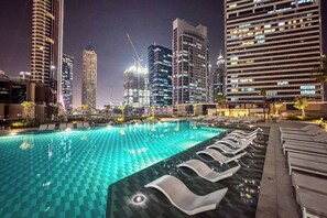 A rooftop pool with lounge chairs, surrounded by high-rise buildings at night. - Elevated 2 Bedroom with Khalifa view in Peninsula (Business Bay)